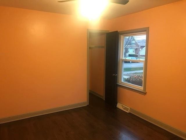 unfurnished room with a ceiling fan, dark wood-style flooring, visible vents, and baseboards