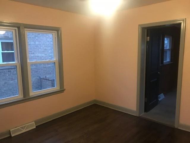 unfurnished room featuring dark wood-type flooring, visible vents, and baseboards