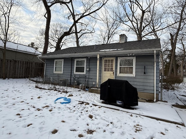 snow covered back of property featuring a garage, a chimney, and fence