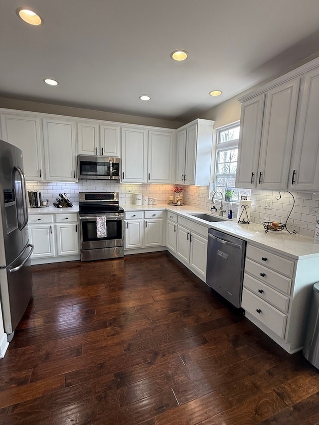 kitchen with appliances with stainless steel finishes, dark wood-type flooring, a sink, and backsplash