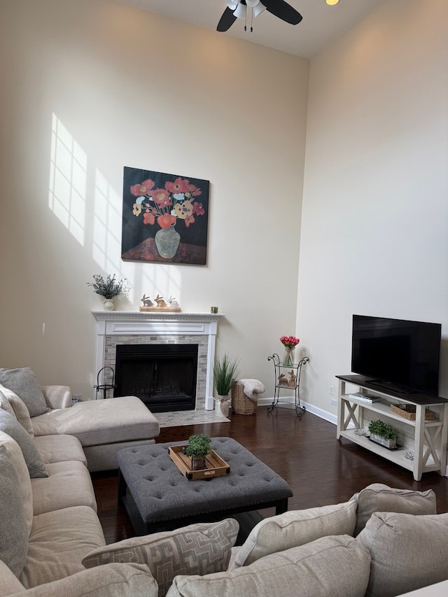 living room with baseboards, a ceiling fan, wood finished floors, a high ceiling, and a fireplace