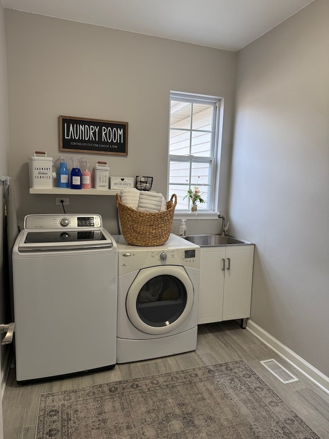 washroom with cabinet space, visible vents, washer and clothes dryer, light wood-style floors, and a sink