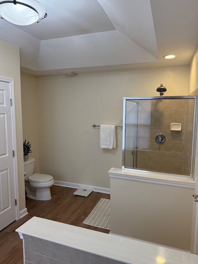 bathroom featuring baseboards, a tile shower, toilet, and wood finished floors