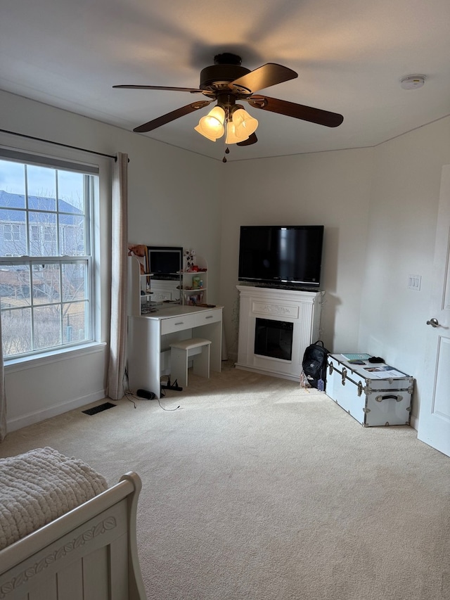 living area with a ceiling fan, a glass covered fireplace, visible vents, and light colored carpet