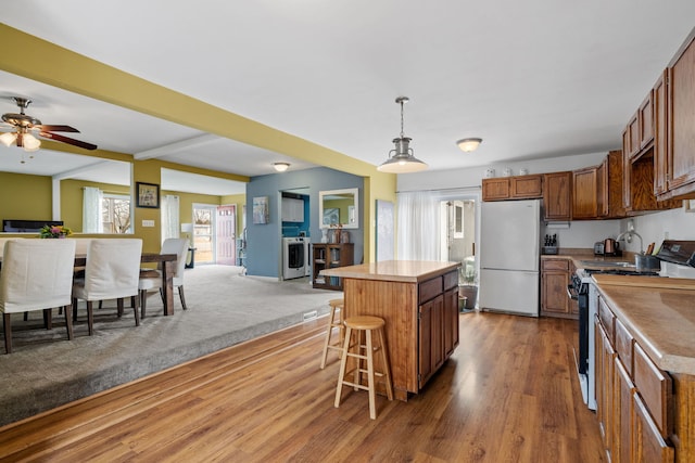 kitchen featuring a center island, freestanding refrigerator, open floor plan, wood finished floors, and range with electric cooktop