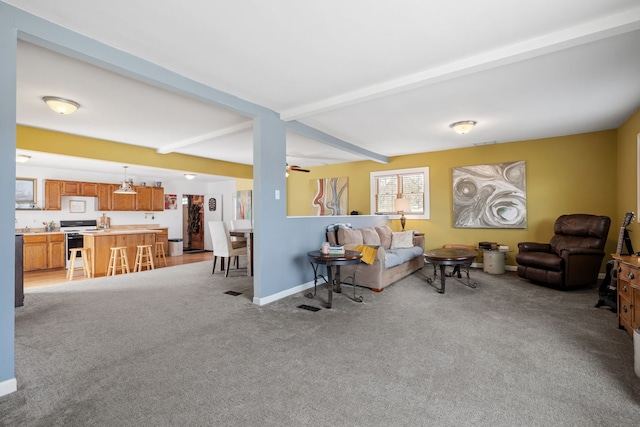 living area featuring light carpet, beamed ceiling, baseboards, and ceiling fan