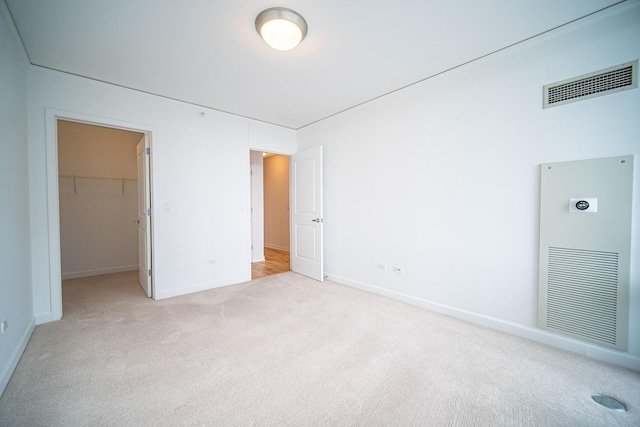 unfurnished bedroom featuring a closet, light colored carpet, visible vents, a spacious closet, and baseboards