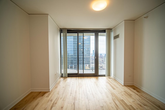 unfurnished room with baseboards, visible vents, floor to ceiling windows, and wood finished floors