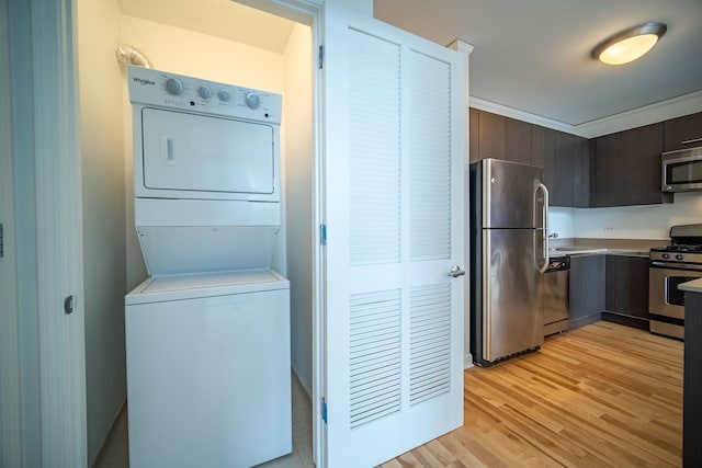 kitchen with stacked washer / drying machine, light wood-style flooring, appliances with stainless steel finishes, dark brown cabinetry, and a sink