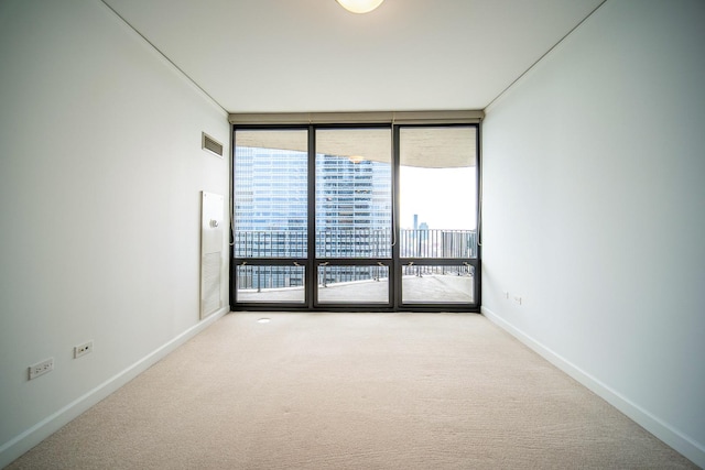 carpeted spare room with floor to ceiling windows, visible vents, and baseboards