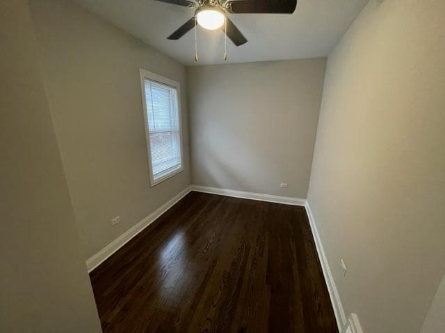 spare room featuring a ceiling fan, baseboards, and dark wood-style flooring