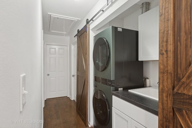 laundry room with a barn door, dark wood-style floors, cabinet space, stacked washer / drying machine, and a sink