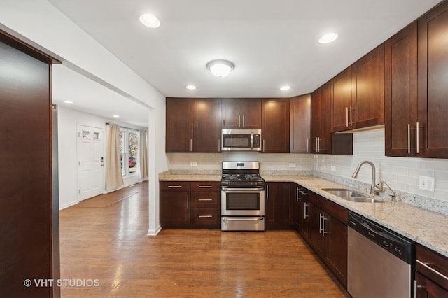 kitchen with wood finished floors, appliances with stainless steel finishes, decorative backsplash, and a sink