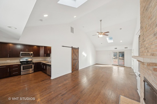 kitchen with a ceiling fan, stainless steel appliances, a barn door, a skylight, and dark brown cabinets