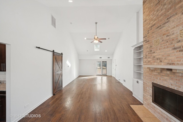 unfurnished living room with a barn door, wood finished floors, visible vents, a ceiling fan, and high vaulted ceiling