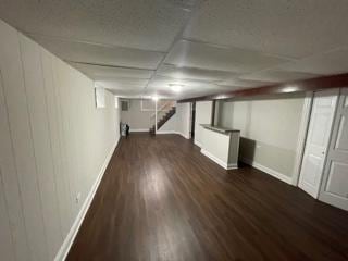 finished basement featuring stairs, a drop ceiling, dark wood-style floors, and baseboards