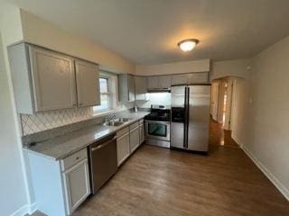 kitchen featuring baseboards, appliances with stainless steel finishes, wood finished floors, gray cabinetry, and a sink