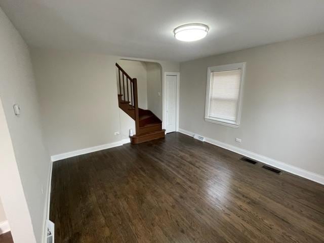 spare room featuring dark wood-type flooring, visible vents, stairway, and baseboards