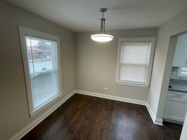 unfurnished dining area featuring dark wood finished floors and baseboards