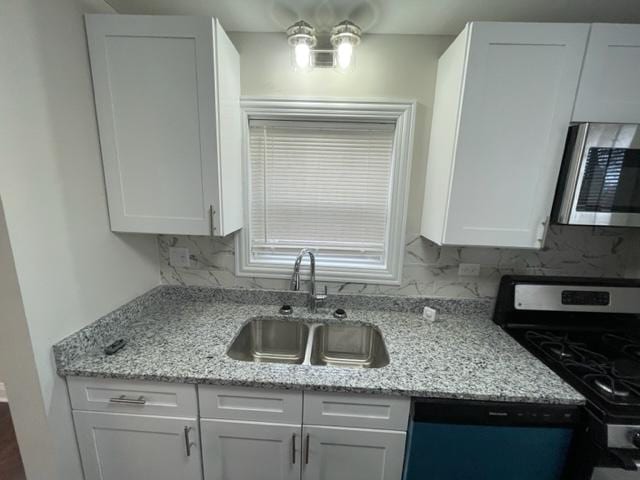 kitchen with tasteful backsplash, white cabinets, light stone counters, appliances with stainless steel finishes, and a sink