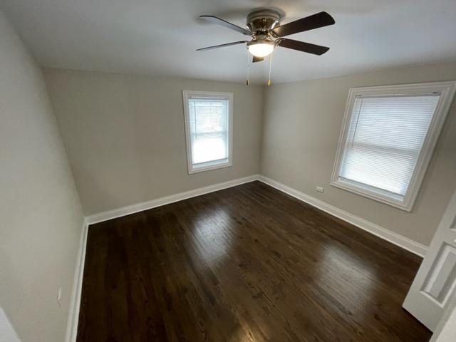 spare room featuring dark wood-type flooring, a ceiling fan, and baseboards