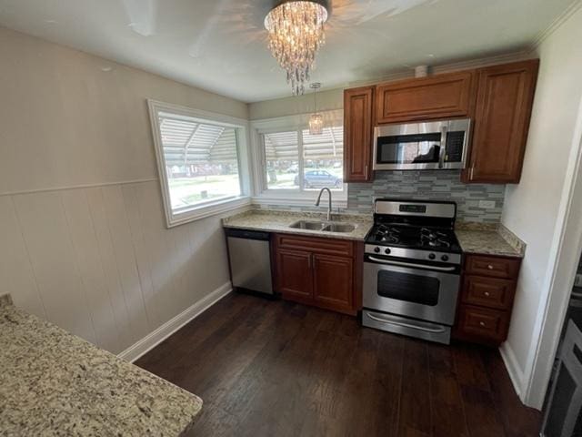 kitchen with brown cabinets, dark wood-type flooring, light stone countertops, stainless steel appliances, and a sink