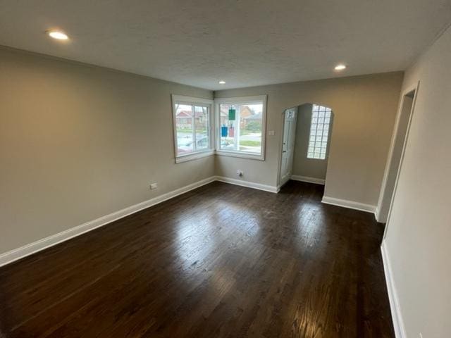 unfurnished room with dark wood-type flooring, arched walkways, baseboards, and recessed lighting