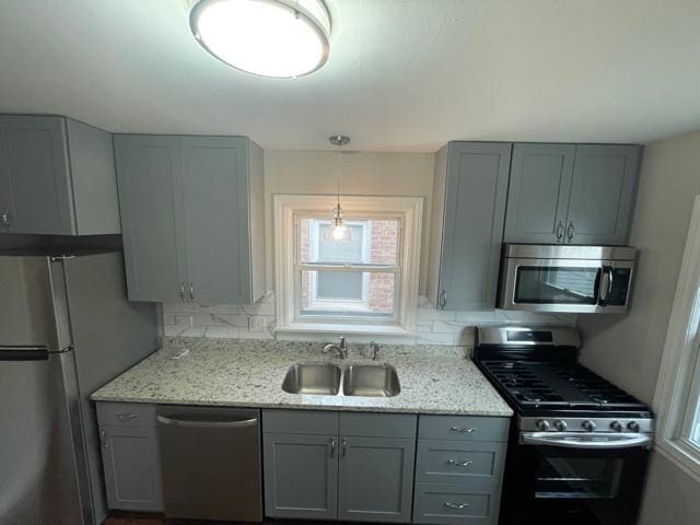 kitchen featuring stainless steel appliances, a sink, gray cabinetry, and light stone countertops