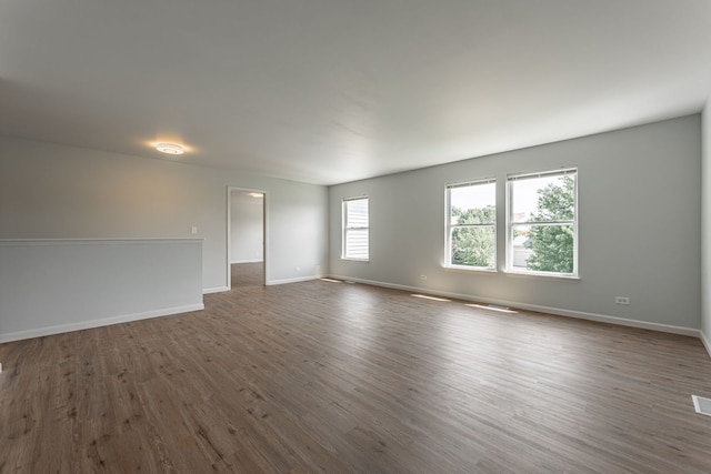 empty room with dark wood-style floors, visible vents, and baseboards