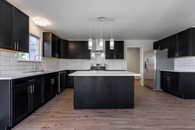 kitchen featuring wall chimney exhaust hood, appliances with stainless steel finishes, decorative light fixtures, light countertops, and a sink