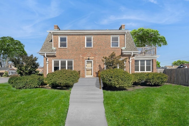 view of front of house featuring brick siding, a shingled roof, a chimney, fence, and a front yard