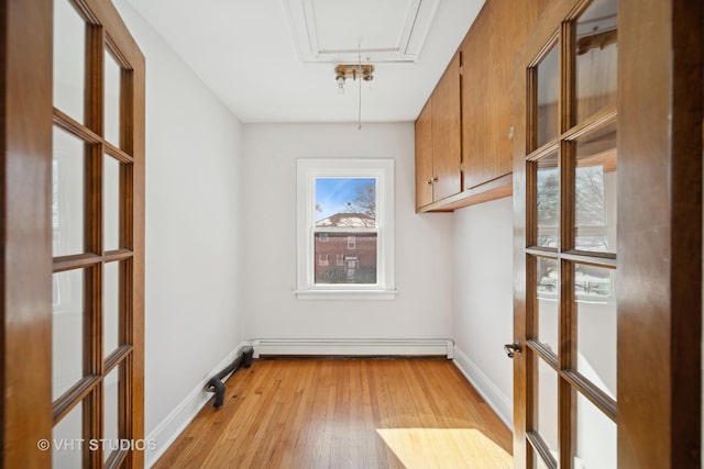 interior space featuring a baseboard radiator, light wood finished floors, attic access, and baseboards