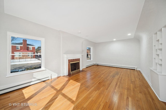 unfurnished living room featuring baseboard heating, a baseboard radiator, hardwood / wood-style flooring, and a brick fireplace