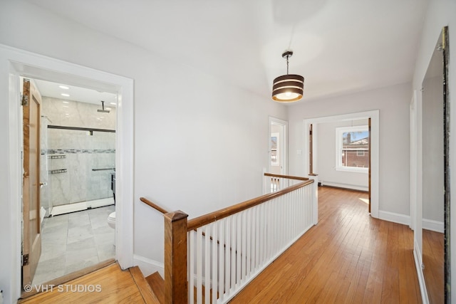 hall with baseboards, baseboard heating, hardwood / wood-style floors, and an upstairs landing