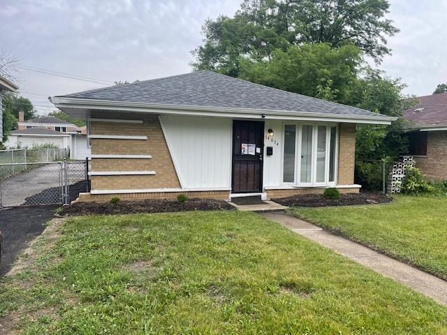 view of front of home featuring a front lawn, roof with shingles, fence, and brick siding