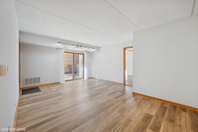 unfurnished room featuring baseboards, light wood-style flooring, visible vents, and a textured ceiling