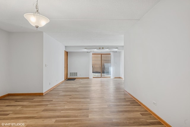 spare room featuring a textured ceiling, light wood finished floors, visible vents, and baseboards