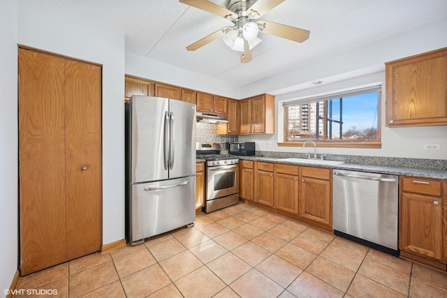 kitchen featuring a ceiling fan, brown cabinets, stainless steel appliances, a sink, and light tile patterned flooring