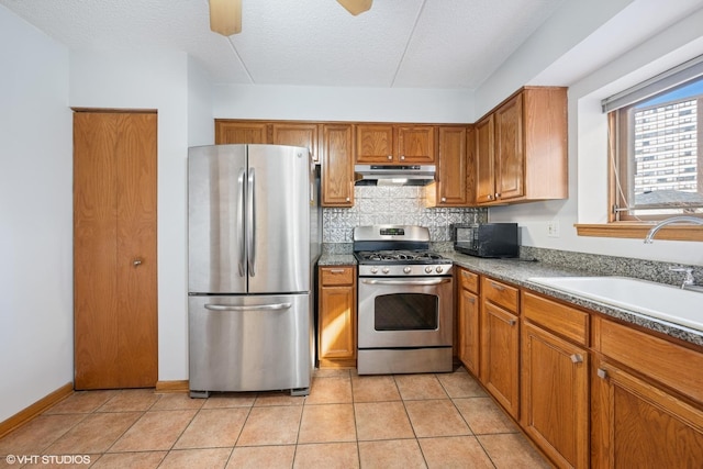 kitchen featuring appliances with stainless steel finishes, brown cabinetry, a sink, and under cabinet range hood