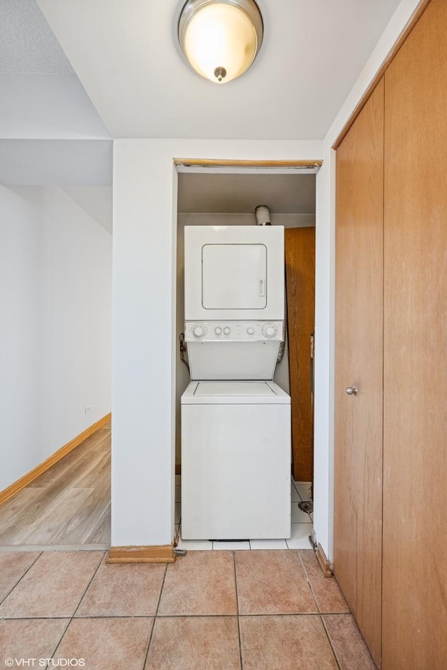 clothes washing area with light tile patterned floors, laundry area, stacked washing maching and dryer, and baseboards