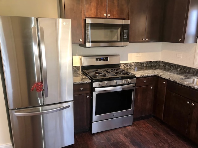 kitchen featuring stainless steel appliances, dark wood-type flooring, dark brown cabinetry, and dark stone countertops