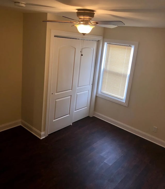 unfurnished bedroom featuring dark wood-type flooring, a closet, ceiling fan, and baseboards