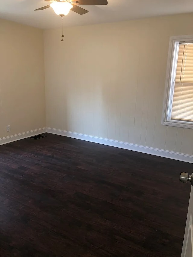 spare room featuring dark wood-style floors, ceiling fan, visible vents, and baseboards