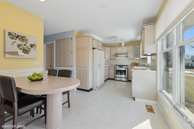 kitchen featuring light brown cabinets, white refrigerator with ice dispenser, stainless steel stove, light countertops, and light floors