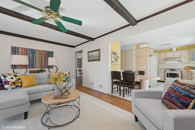 living area with visible vents, ceiling fan, beamed ceiling, light wood-type flooring, and ornamental molding