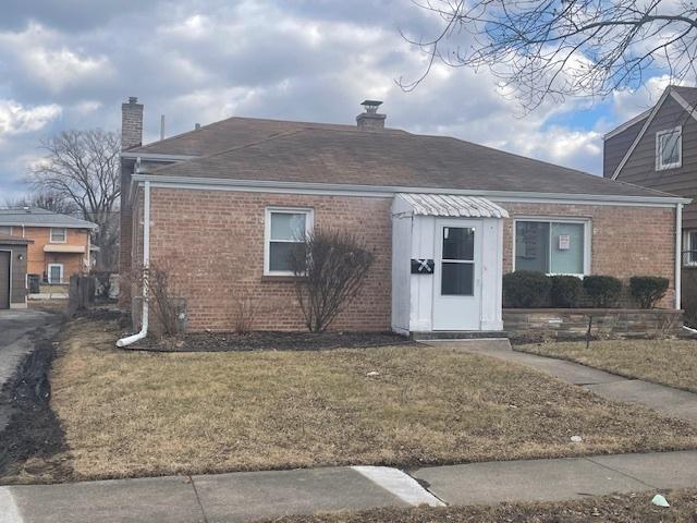 view of front of home featuring a shingled roof, brick siding, a chimney, and a front lawn