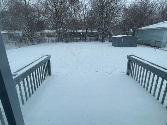 yard covered in snow featuring an outbuilding, a shed, and fence