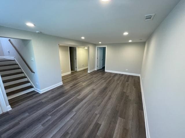 empty room featuring dark wood-style flooring, visible vents, baseboards, and stairs