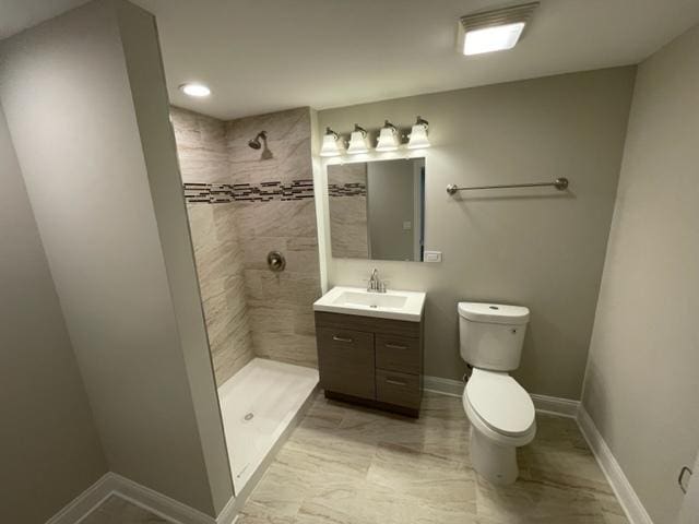 bathroom with toilet, baseboards, tiled shower, and vanity