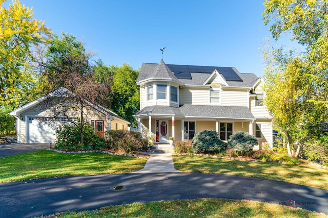 victorian house featuring a porch, a garage, solar panels, a shingled roof, and a front yard